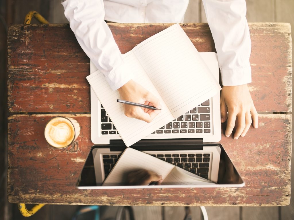 Man writing in notebook and working on laptop