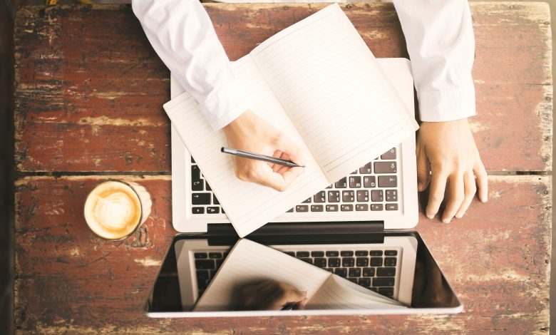 Man writing in notebook and working on laptop